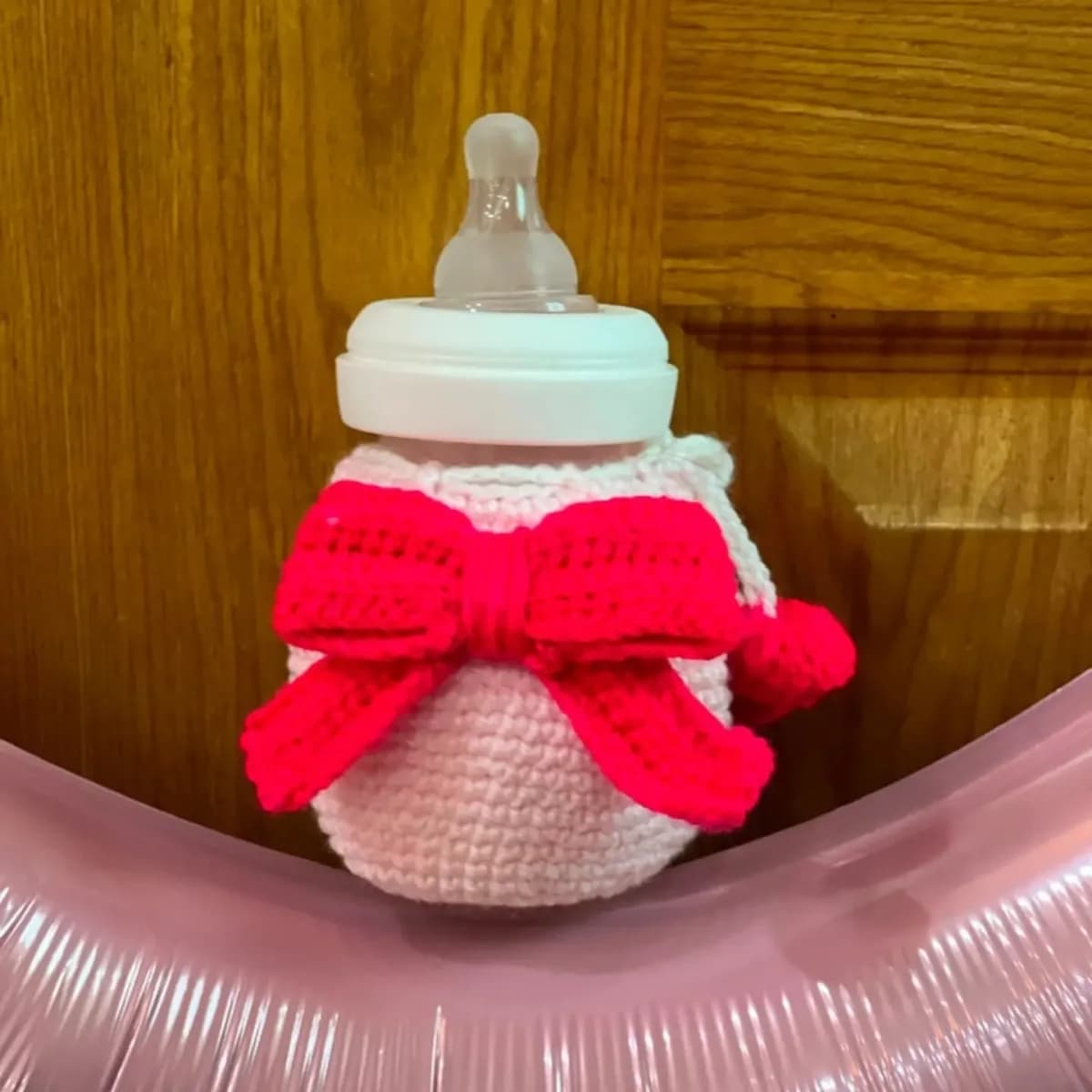Pink crochet baby-bottle cover with a bright pink bow