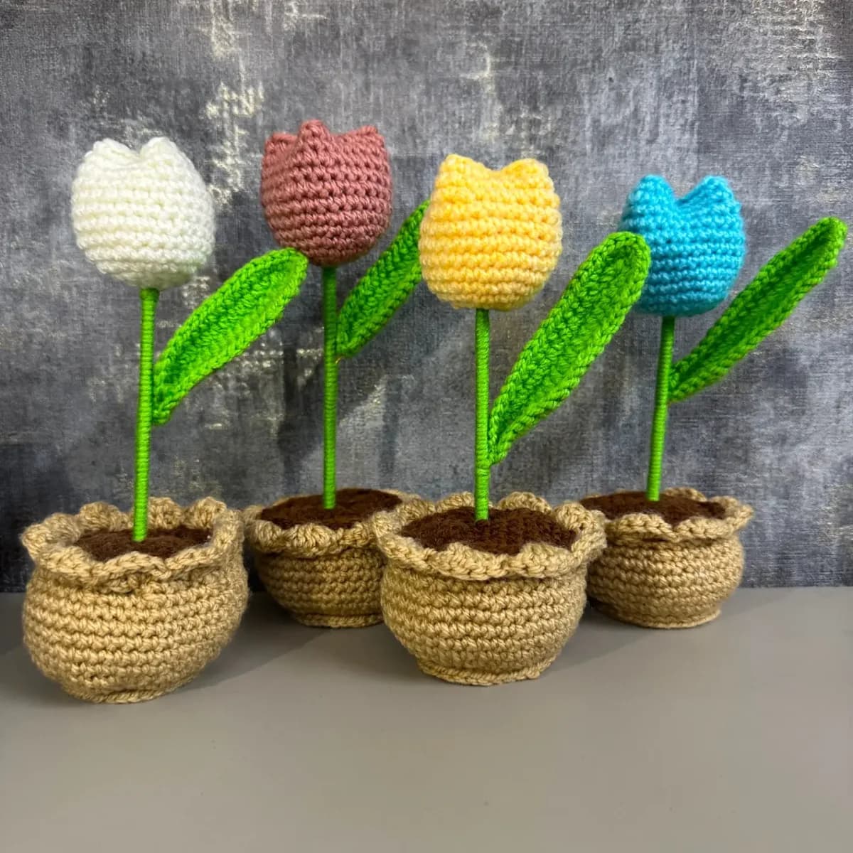 A collection of colourful crochet tulips in small woven pots